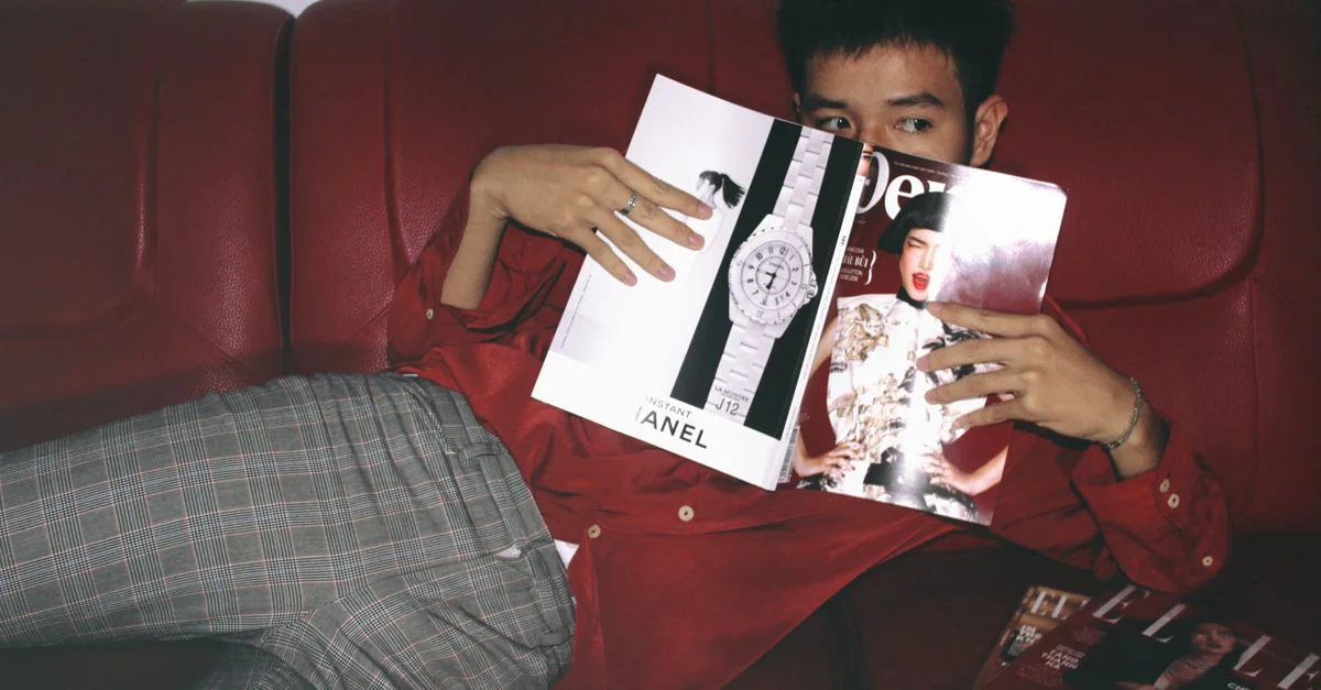 Un homme élégant se détend sur un canapé rouge tout en lisant des magazines de mode à l'intérieur.