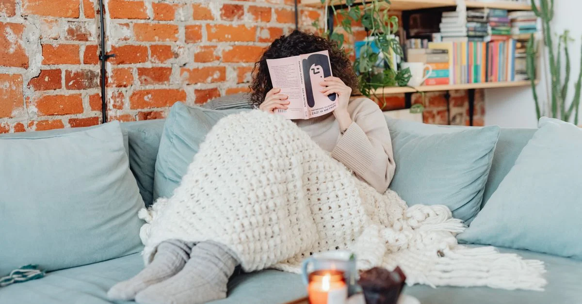 Femme se relaxant avec un livre sur un canapé confortable, entourée d'une lumière douce et chaleureuse.