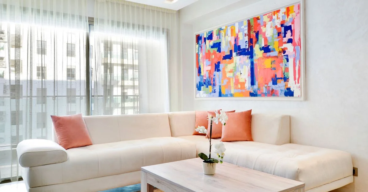 Salon lumineux et moderne avec des œuvres d'art abstraites, un canapé neutre et une plante d'intérieur sur la table basse.