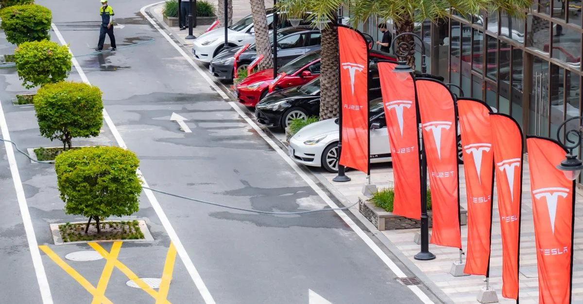 Vue aérienne de plusieurs voitures Tesla stationnées le long de drapeaux de marque dans une rue de la ville.