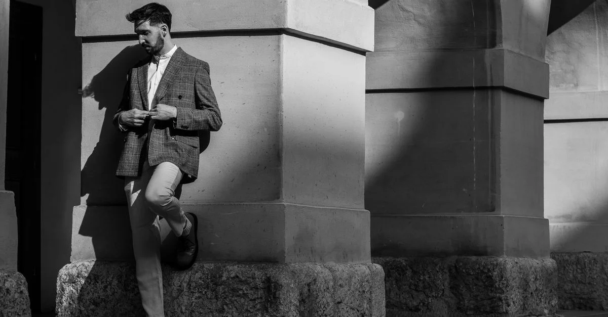 Photo en noir et blanc d'un homme élégant en costume appuyé contre un bâtiment historique à Graz.