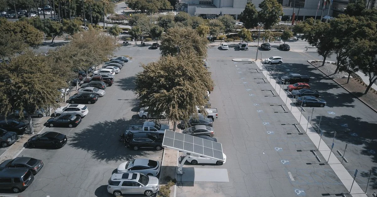 Vue en plongée d'un parking avec des panneaux solaires et des véhicules garés, entouré de verdure.