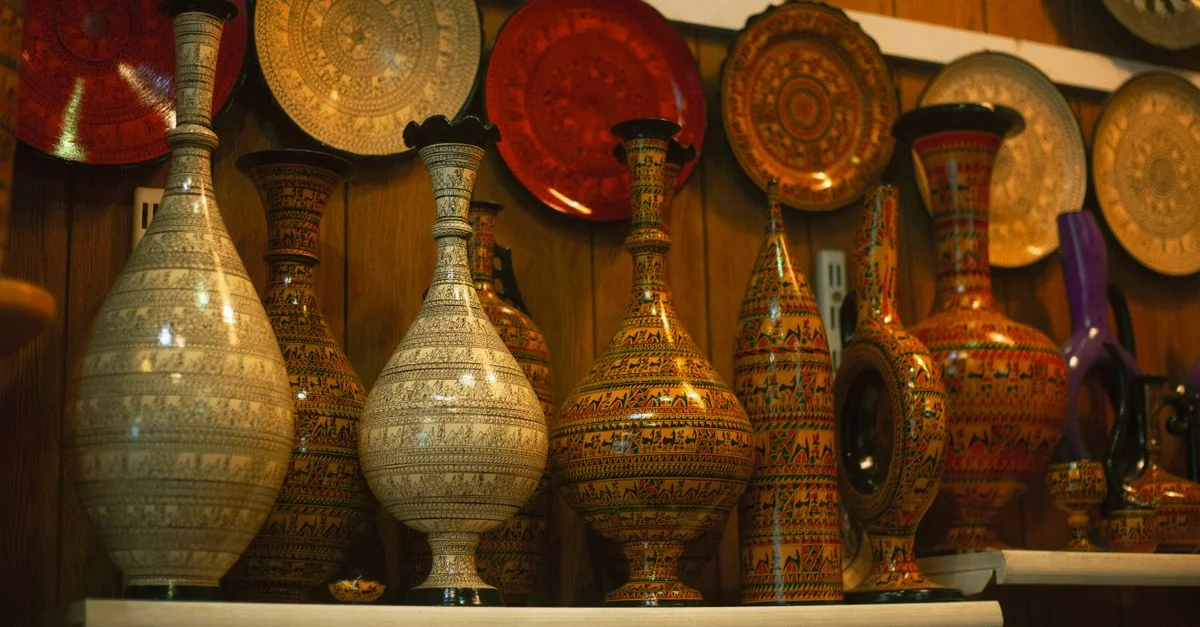 Vue détaillée de vases et assiettes magnifiquement fabriqués à la main, mettant en valeur des designs complexes et des couleurs vives sur une étagère en bois.