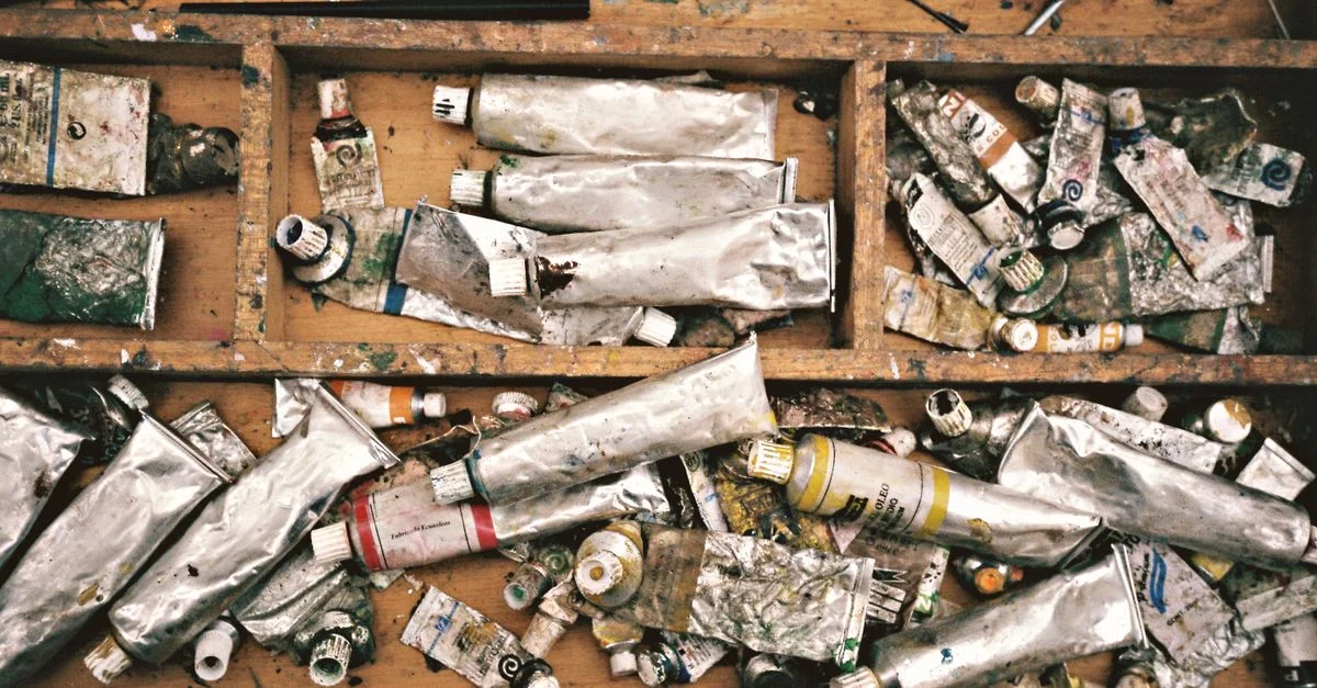 Un tiroir rustique en bois rempli de tubes de peinture pressés, de pinceaux et d'outils artistiques, témoignant de la créativité.
