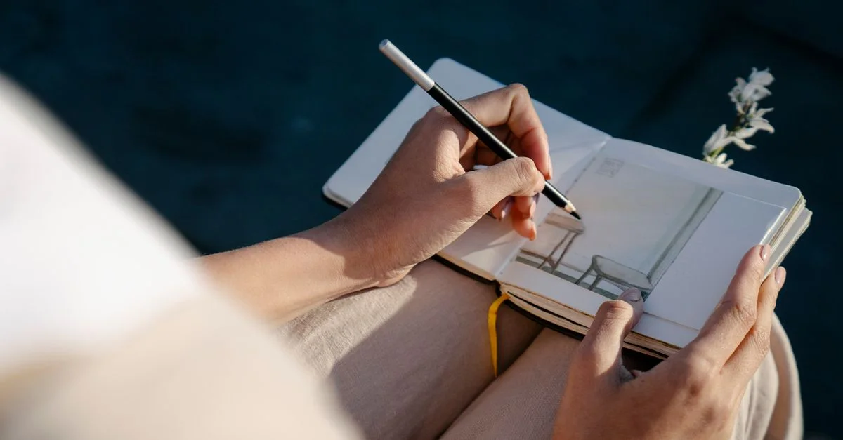 Un artiste esquissant une scène dans un carnet sous la lumière du soleil, créant une ambiance sereine et créative.