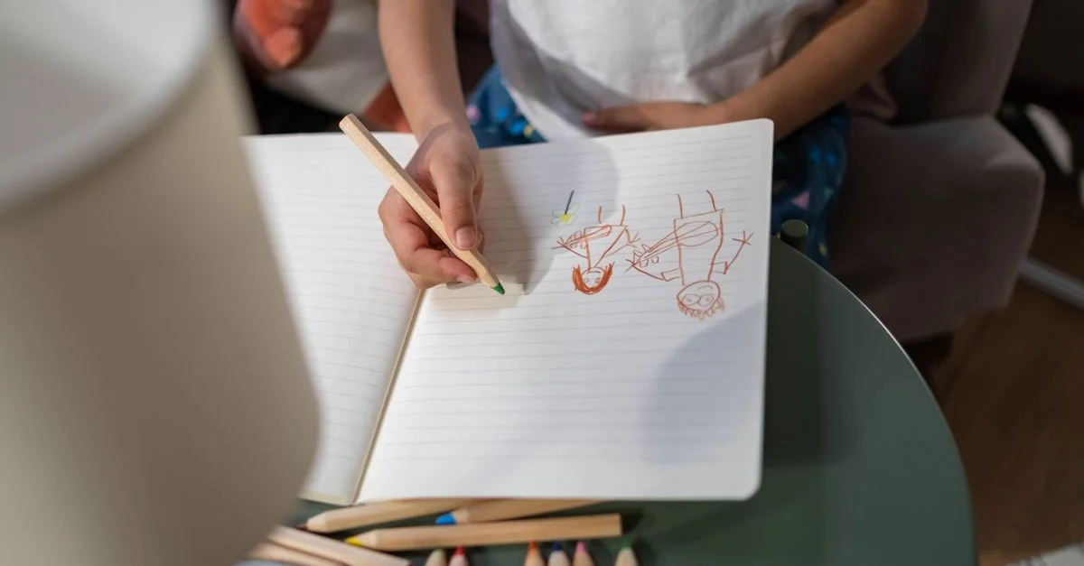 Une jeune enfant dessine dans un carnet avec des crayons de couleur, jeu créatif à l'intérieur.