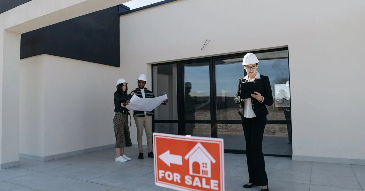 Agents immobiliers en casques de chantier examinant des plans à côté d'une maison à vendre.
