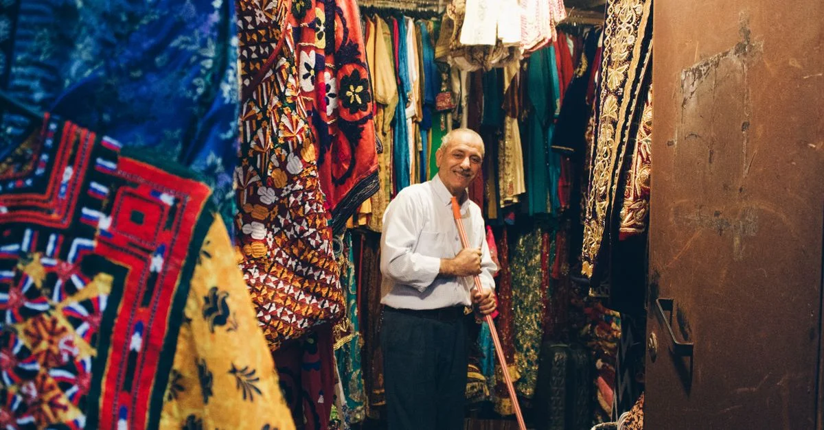 Marchand âgé dans un bazar vibrant avec des tissus colorés autour de lui.