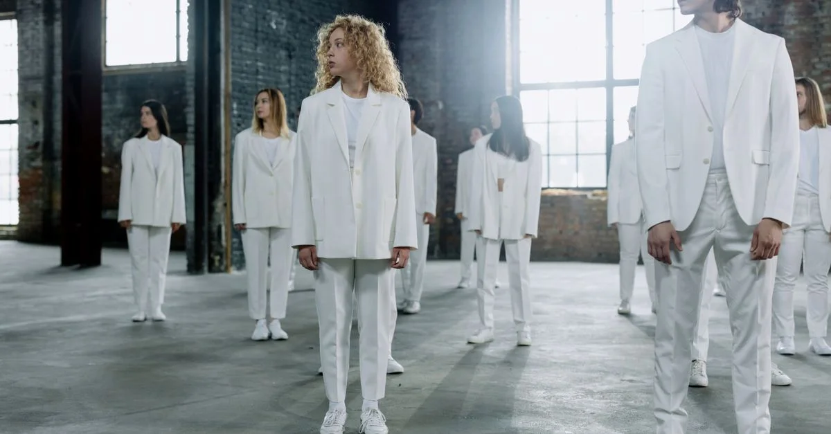 Un groupe diversifié d'adultes en costumes blancs se tient à l'intérieur d'un grand espace industriel, créant une scène conceptuelle.